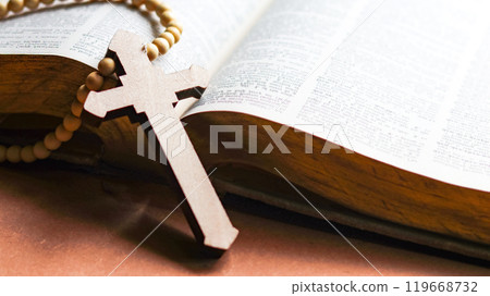 Brown wooden cross on an old open book symbolizing the spread of Jesus Christs love among Christians reflecting faith devotion and the importance of Christian teachings. 119668732