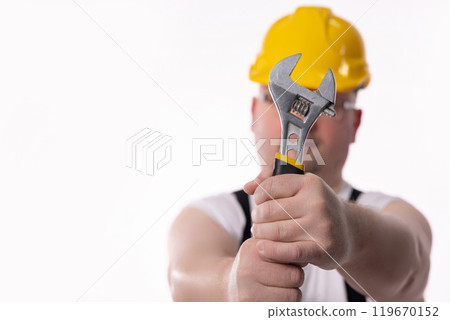 A diligent worker uses an adjustable wrench, dressed in proper safety gear for the job 119670152