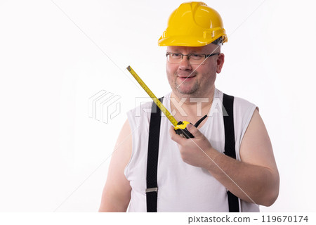 A diligent Construction Worker using a Measuring Tape and wearing a Hard Hat for safety on site A diligent Construction Worker using a Measuring Tape and wearing a Hard Hat for safety on site 119670174