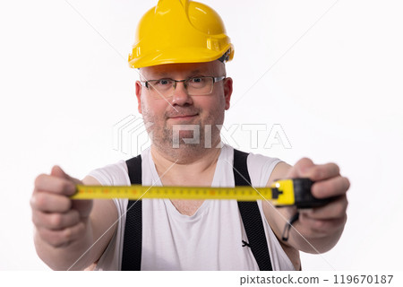 A construction worker is meticulously measuring with a tape measure for his project A construction worker is meticulously measuring with a tape measure for his project 119670187
