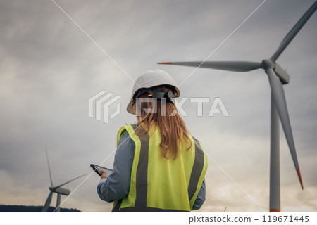 Wind Energy Technician Monitoring Turbines with Tablet in Renewable Energy Field 119671445
