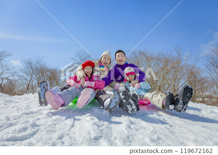A family of four sledding in a snowy park 119672162