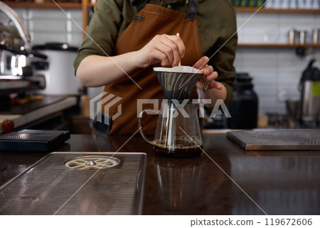 Woman barista using stainless steel funnel for coffee filtration 119672606