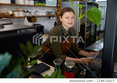 Young woman barista with mobile tablet at coffee shop counter desk 119672623