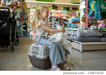 Attractive little girl with dog posing on plastic transportation carriage at pet shop Attractive little girl with dog posing on plastic transportation carriage at pet shop 119672638