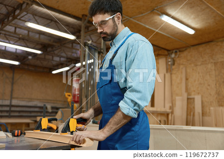 Carpenter fixing wooden plank on workbench with clamps at craft woodwork studio 119672737