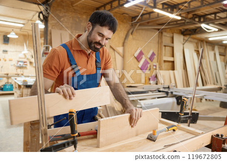 Male artisan worker holding and assembling pieces of wood using glue 119672805