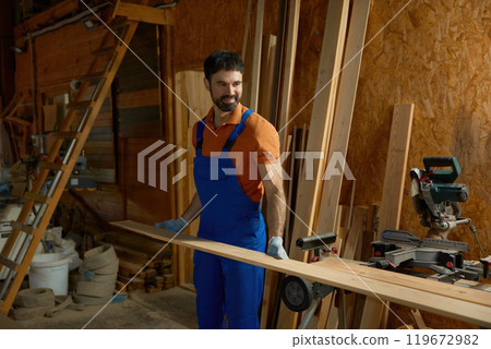 Young man carpenter in uniform putting wood plank on modern equipment Young man carpenter in uniform putting wood plank on modern equipment 119672982