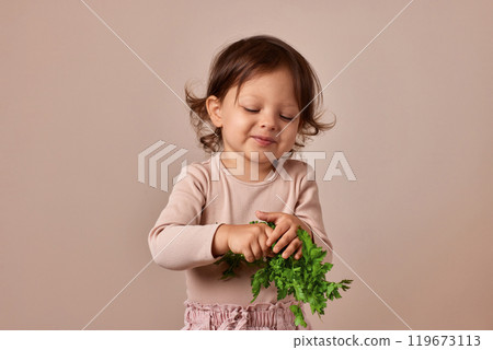 smiling child girl holding fresh green parsley on beige background. healthy baby food. 119673113