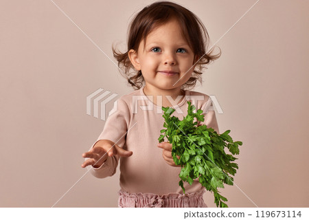 cute child girl holding fresh green parsley on beige background. healthy baby food. 119673114