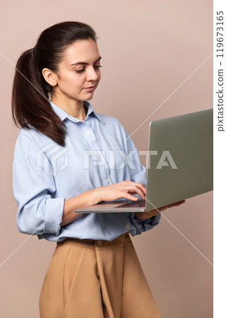 pretty freelancer business woman in blue shirt using laptop for work, e-learning, e-banking or online shopping on beige background pretty freelancer business woman in blue shirt using laptop for work, e-learning, e-banking or online shopping on beige background 119673165