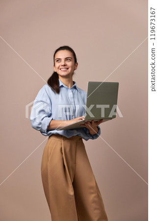 smiling pretty freelancer business woman in blue shirt using laptop for work, e-learning, e-banking or online shopping on beige background smiling pretty freelancer business woman in blue shirt using laptop for work, e-learning, e-banking or online shopping on beige background 119673167