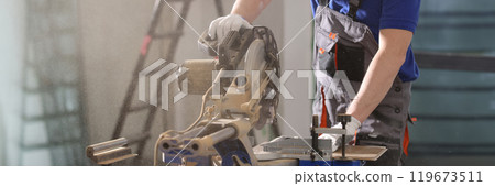 Worker in uniform cuts timber with sawing machine in shop 119673511