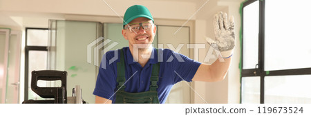Employee waves hand standing by sawing machine in room 119673524