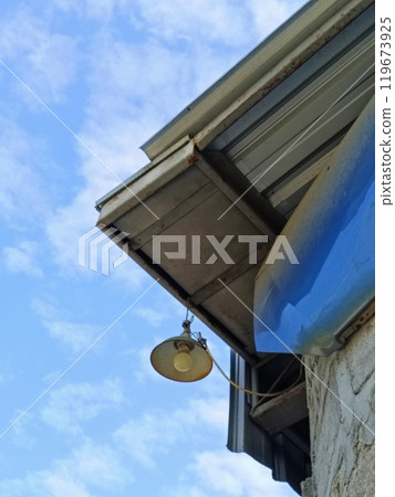 A lamp hanging under a roof. The sky's blue filled with clouds. A lamp hanging under a roof. The sky's blue filled with clouds. 119673925