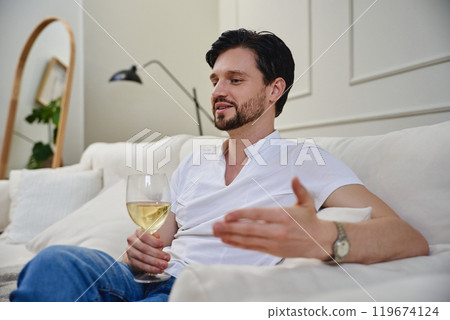 Young man enjoying a glass of white wine while relaxing on a sofa at home Young man enjoying a glass of white wine while relaxing on a sofa at home 119674124