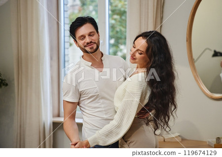 Couple dancing together in a cozy living room during a sunny afternoon Couple dancing together in a cozy living room during a sunny afternoon 119674129