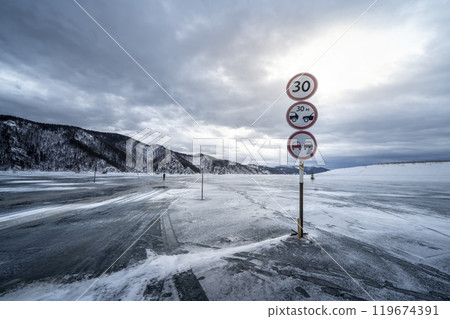 Ice winter crossing in Russia on the Yenisei River in Siberia Near Krasnoyarsk and Divnogorsk. A winter landscape featuring a frozen roadway with traffic signs in a frosty environment 119674391