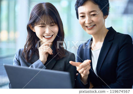 Two businesswomen in suits having a meeting while looking at a computer 119674567
