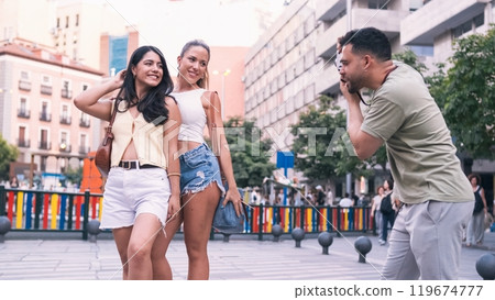 Man photographing stylish female friends on street in city 119674777