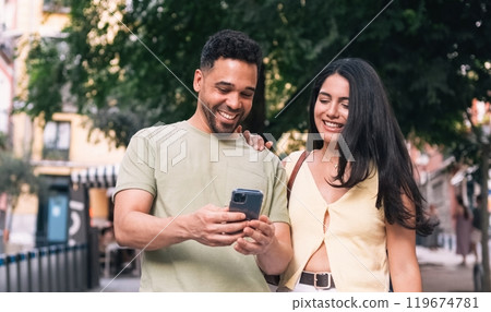 Happy couple using mobile phone on street in city Happy couple using mobile phone on street in city 119674781