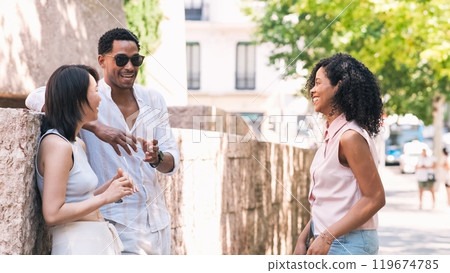 Diverse friends talking on sidewalk along wall in city Diverse friends talking on sidewalk along wall in city 119674785