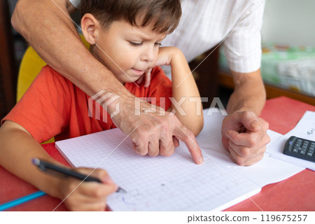 A junior schoolboy does his homework with the help of his father. 119675257