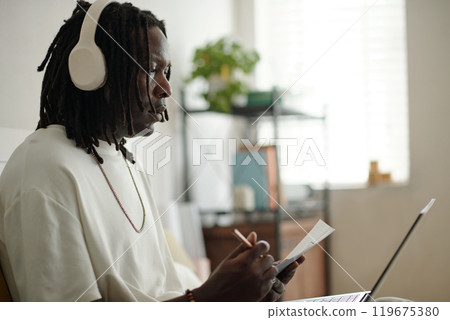 Young Man Listening to Music While Writing Notes 119675380