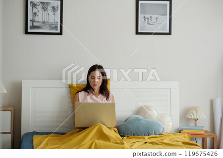 Young Woman Using Laptop in Cozy Bedroom Setting 119675426