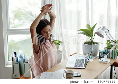 Woman Stretching at Desk in Sunlit Home Office 119675455