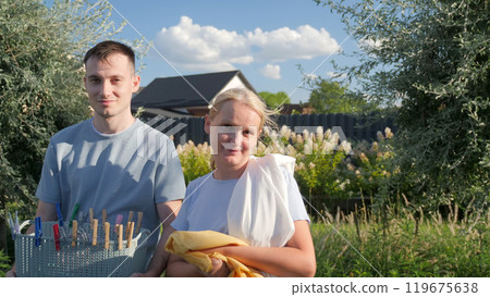 Young man and middle-aged woman smiling as they hold laundry essentials in a garden, creating a warm family atmosphere on a sunny day. 119675638