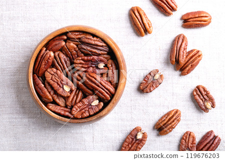 Pecan halves in a wooden bowl on linen fabric. Shelled and dried pecan nuts, seeds and fruits of Carya illinoinensis. Ready to eat fresh or roasted as snack, and used for baking. Close-up from above. 119676203