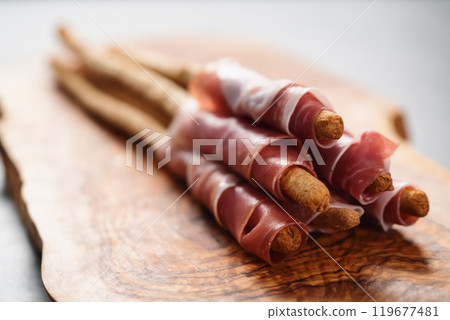 Grissini with prosciutto on olive wood board 119677481