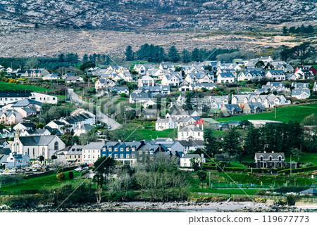 A coastal town with a diverse array of houses, a church, and a small harbor in the foreground. The town is surrounded by lush greenery and a rocky hill in the background. A coastal town with a diverse array of houses, a church, and a small harbor in the foreground. The town is surrounded by lush greenery and a rocky hill in the background. 119677773