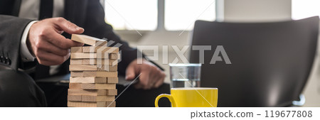 Wide panorama view of businessman in office building a tower of stacked blocks 119677808