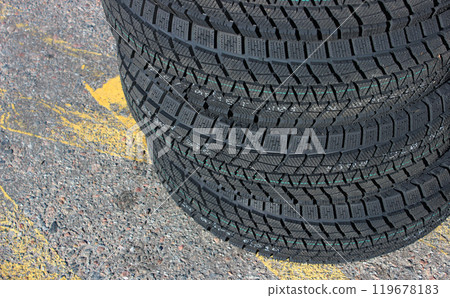 Identical winter tires with aggressive tread patterns are stacked on the highway. Same studless tires stock photo 119678183
