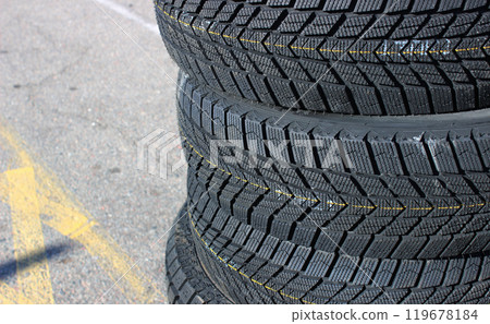 A set of four new winter tires are stacked on asphalt before the seasonal tire change. Same tread pattern tires detailed image 119678184
