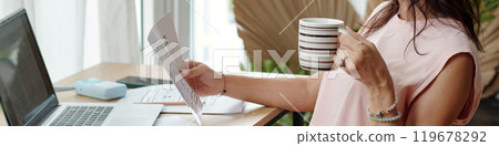 Examining Document While Holding Coffee Mug at Desk 119678292