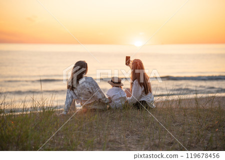 Back view of two caucasian female friends and a child making selfie at sunset on the Baltic seashore 119678456