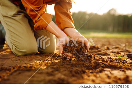 Young female farmer's hands touch dry soil in an agricultural field. Gardening and ecology concept. 119679308