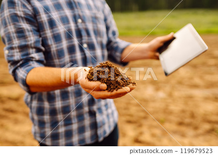 Farmer in a sunny field collects soil, checks its health using a digital tablet. Technology concept Farmer in a sunny field collects soil, checks its health using a digital tablet. Technology concept 119679523