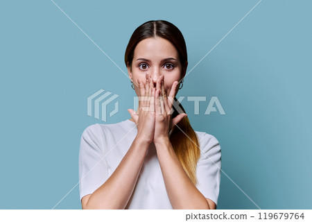 Surprised beautiful young woman covering her open mouth with hands, on blue background 119679764