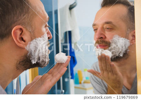 Guy shaving his beard in bathroom Guy shaving his beard in bathroom 119679869