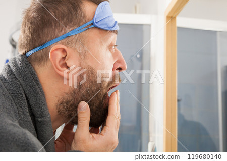 Sleepy man looking at mirror and yawning Sleepy man looking at mirror and yawning 119680140