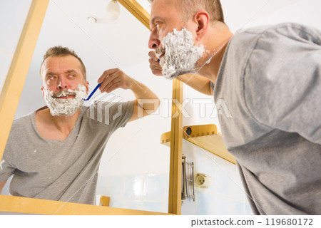 Guy shaving his beard in bathroom Guy shaving his beard in bathroom 119680172