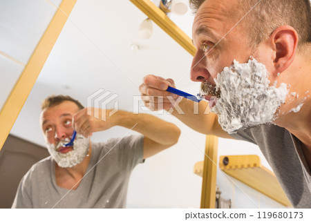 Guy shaving his beard in bathroom Guy shaving his beard in bathroom 119680173