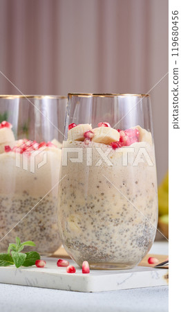 A glass of chia seeds and yogurt, with banana pieces and pomegranate seeds added to the dessert 119680456