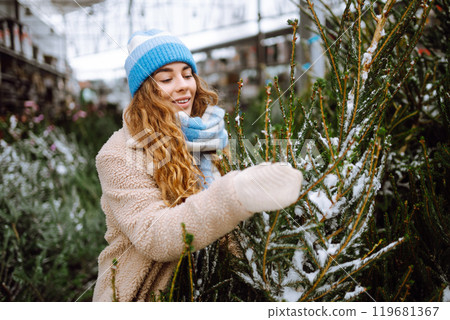 Smiling woman in warm clothes chooses a Christmas tree at the market. Holiday concept. 119681367
