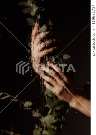Close up of two hands holding a leafy green plant behind glass with water drops running down it. Close up of two hands holding a leafy green plant behind glass with water drops running down it. 119681784