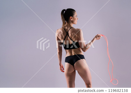 Healthy young woman skipping rope in studio. Muscular young female exercising with jumping rope Healthy young woman skipping rope in studio. Muscular young female exercising with jumping rope 119682138